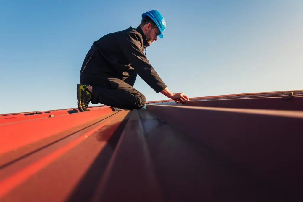 Roofing contractor inspecting standing seam metal roof while wearing blue hard hat