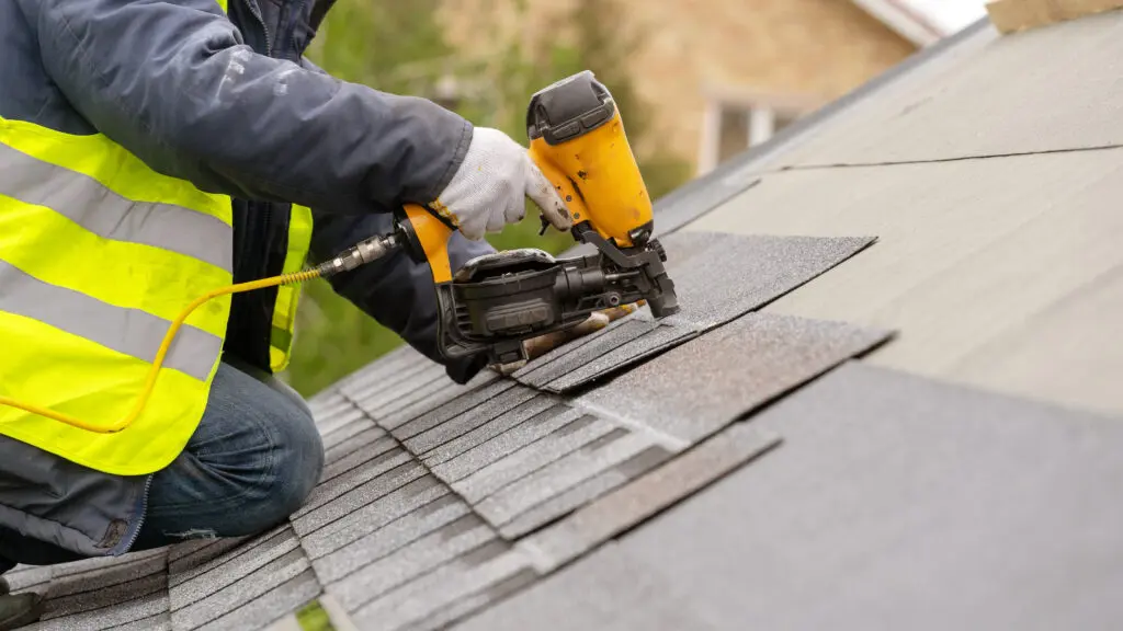 roofer using nail gun to install asphalt shingles