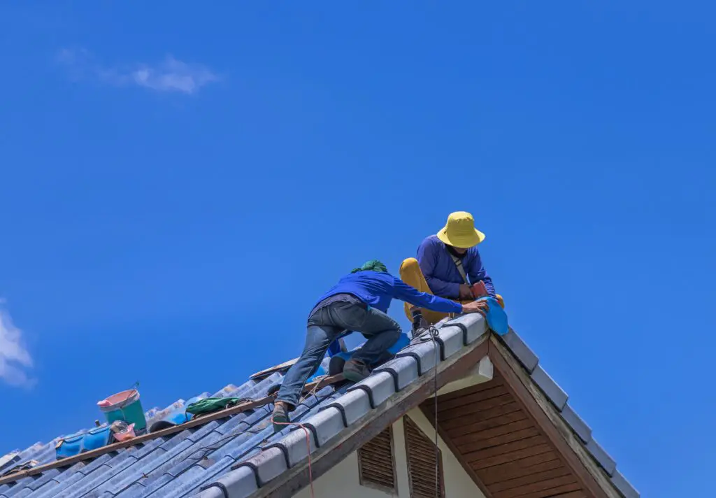 Roofing contractors working on tiled residential roof under bright blue sky in Omaha
